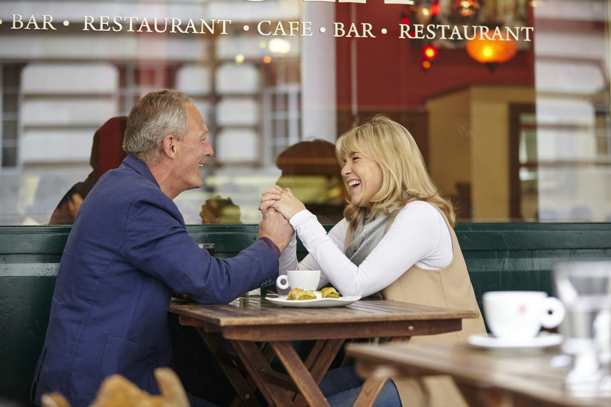 Mature dating couple holding hands at sidewalk cafe table